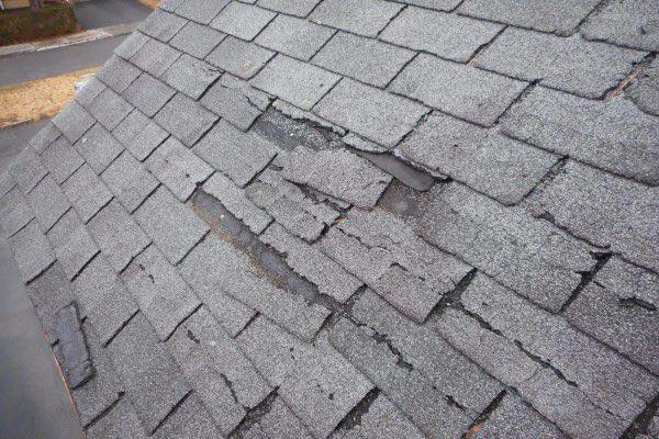 close up of damaged shingles on a roof. shingles are broken, some are missing